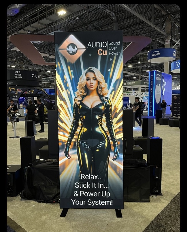 marketing image at a trade show featuring a conventionally attractive woman in an inappropriate outfit with sexually implied text at the bottom