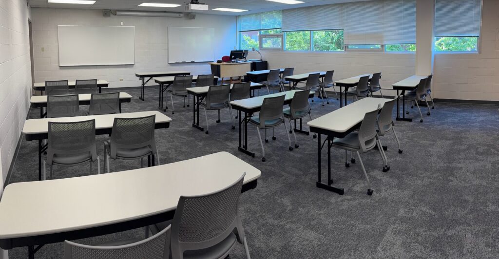 Rows of tables looking on two white boards and a projector